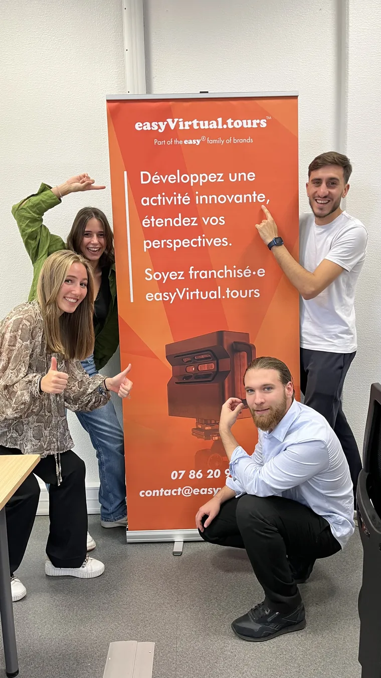 Quatre membres de l'équipe posent en riant autour d'un kakémono easyVirtual.tours