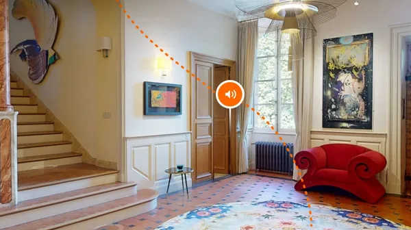 Hall d'un château avec escalier, fauteuil rouge et tableaux, point audio de la visite