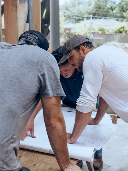 A construction team leaning over plans spread out on a table